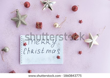  Holiday decorations and notebook with New Year lettering on pink background top view, Christmas planning concept. Flat style. High quality photo