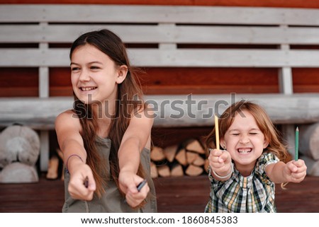 Two smiling girls are sitting outdoors near a wooden house and are drawing. Child with pencils for drawing in hands. Art and drawing concept.