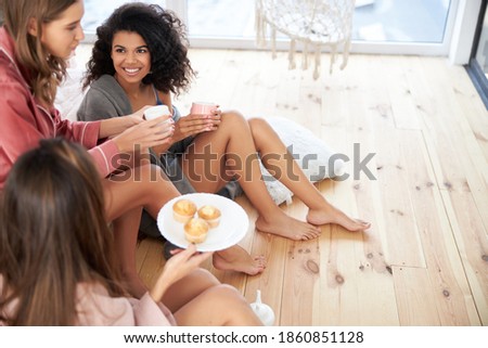 Three best friends discussing something while drinking tea and eating cupcakes at the floor. Stock photo