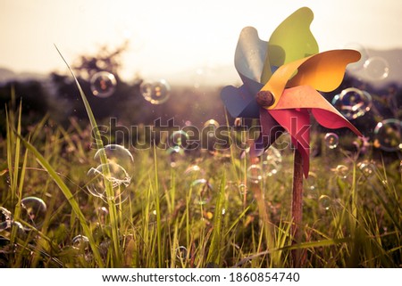 Colorful pinwheel with blowing bubbles in a green field with sunset in the background Royalty-Free Stock Photo #1860854740