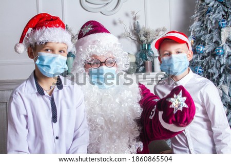 Santa Claus and two boys in N95 Face Mask during coronavirus quarantine in a red cap and with a big curly white beard, glasses near the New Year tree, an animator in a Santa carnival costume.
