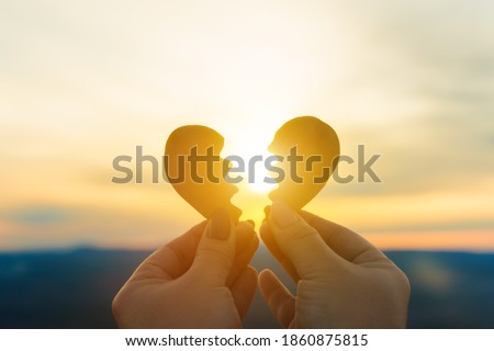 Two hands hold a broken heart on the background of the sunset. Concept spat divorce dissolution, love feelings Royalty-Free Stock Photo #1860875815