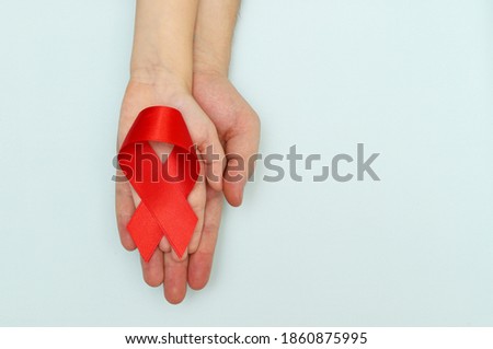 Red ribbon-symbol of world AIDS Day in Caucasian children's and men's hands on a blue background.Copy space