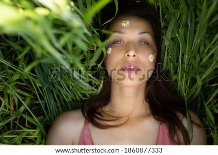beautiful attractive caucasian woman lies in green wheat field looking at camera with wild flowers and daisy glued on her face. Natural cosmetic and wellness idea. skincare, Women Health concept