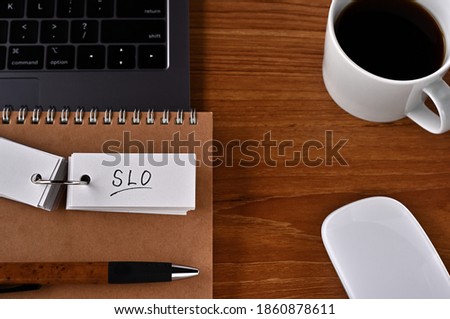 There's a cup of coffee, a laptop and a notebook with a word book on it that says SLO. It was an abbreviation for Service Level Objective.