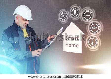 Smart home with an engineer on a gray background. Builder looks at the floor plan and information in the tablet against the background of smart home labels. Connecting and managing home automation.