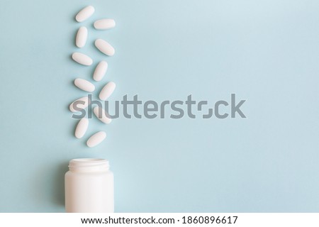 White pills and capsules spilled out of white bottle on light blue background. Minimal medical concept. Pharmaceutical, Covid-19 or Coronavirus. Flat lay, top view, copy space Royalty-Free Stock Photo #1860896617