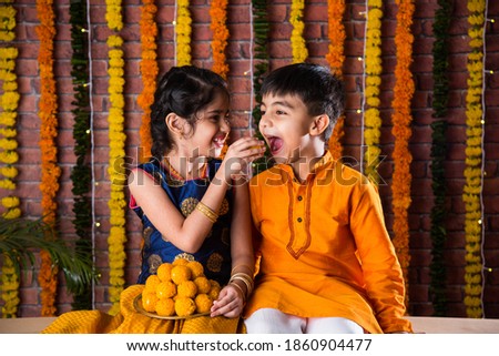 Indian kids, little brother and sister celebrating Diwali, Raksha Bandhan, Bhai Dooj with big gift box and sweet laddoo Royalty-Free Stock Photo #1860904477