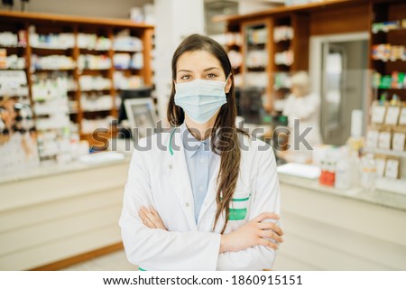 Friendly pharmacist working in a pharmacy amid coronavirus pandemic.Pharmaceutical health care professional providing COVID-19 therapy support.MPharm ina a drugstore wearing a protective face mask Royalty-Free Stock Photo #1860915151