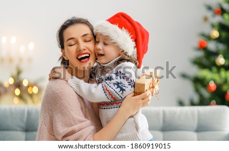 Merry Christmas and Happy Holidays! Cheerful mom and her cute daughter girl exchanging gifts. Parent and little child having fun near tree indoors. Loving family with presents in room.   