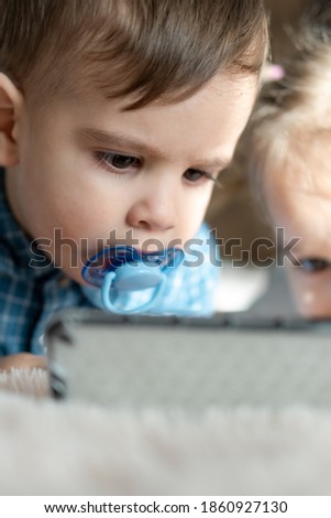 friendship, childhood, technology concepts - two minor children of different nationalities Persian and Slavic appearance watch cartoon on smartphone on bed. kid with pacifier speak by video conference