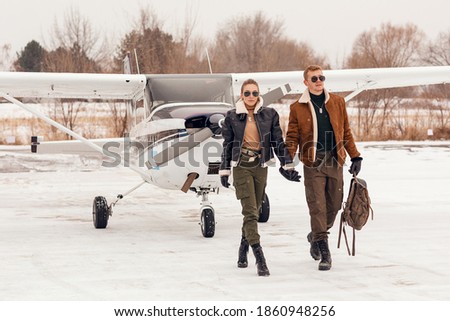 A beautiful, young, stylish couple in winter clothes on a snow-covered runway near a small pleasure plane. 