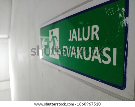 evacuation arrow sign "Jalur Evakuasi" or Evacuation Route attached to the white wall