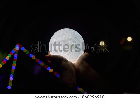 A picture of a hand holding a model of the moon at night and bokeh