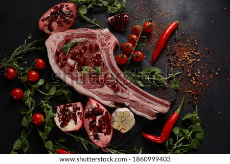 Fresh Raw Beef bone rib steak on black board with herbs and spices