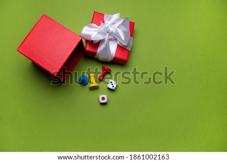 Open red gift box with white ribbon on green background next to three game chips of different colors: red, blue and yellow, Christmas background
