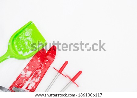 Children's red skis with sticks and a green snow shovel-layout in the snow. Winter outdoor activities, family fun. White natural frosty background. Copy space