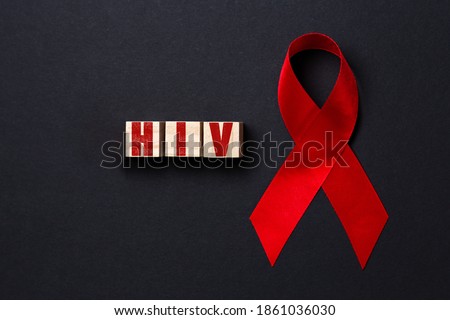 Red ribbon and wooden cubes with the word HIV on a black background. Close up. Flat lay. The concept of world AIDS day