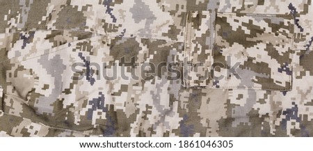 Fragment of pants made of pixellated digital camouflage fabric of dull olive-green color with two different pockets, background

