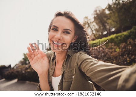 Photo of positive lovely young girl shooting selfie waving palm wear brown shirt park street outdoors