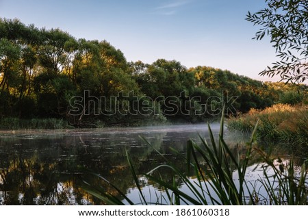 Summer or autumn sunrise over the river. Calm water flow, morning fog and birds. Natural beauty of pristine nature. Water protection zone. Beautiful landscape banner, postcard or desktop wallpaper.