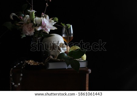 Close up still life picture inspired by 17th century Dutch painting. There are flowers, fruits, jewelry, a glass of wine and a skull on wooden table, in front of a black background. 