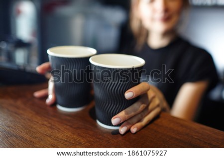 
Barista holds two disposable paper cups of coffee in coffee shop. Blurred image, selective focus