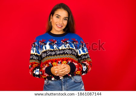 Business Concept - Portrait of Young beautiful Hispanic woman wearing winter sweater against red wall holding hands with confident face.