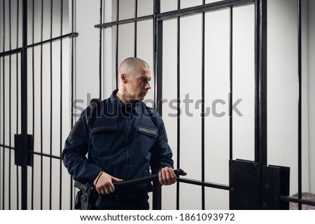 A strict prison guard in uniform guards cells with prisoners in a maximum security prison Royalty-Free Stock Photo #1861093972