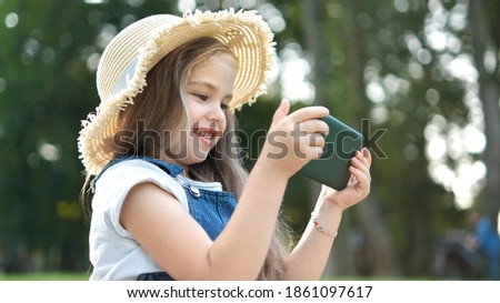 Happy smiling child girl watching in her mobile phone outdoors in summer.