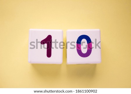 Close-up photo of a white plastic cube with a violet number 10 on a yellow background. Object in the center of the photo