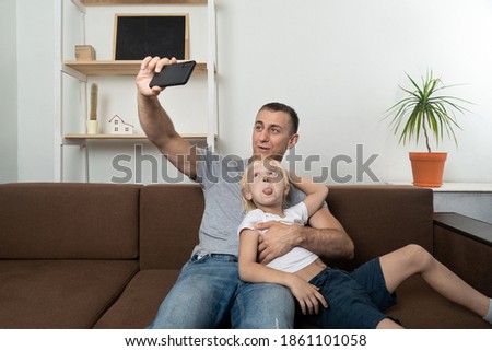 Young father taking selfie with his son sitting and making faces. Father and son having fun together