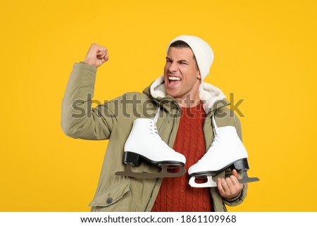 Emotional man with ice skates on yellow background
