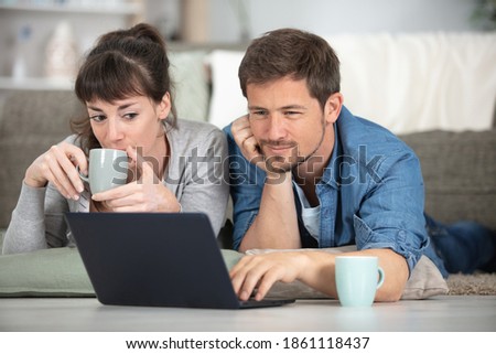 couple layed on floor drinking coffee and looking at laptop