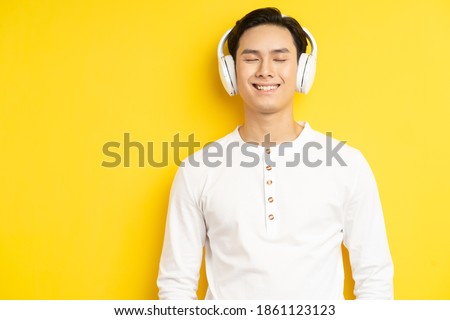 Photo of Asian man in white shirt listening to music with his eyes closed on yellow background
