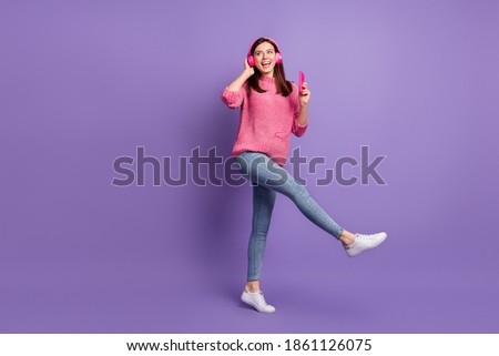 Full length body size photo of girl in earphones with mobile phone dancing kicking smiling isolated on vivid violet color background
