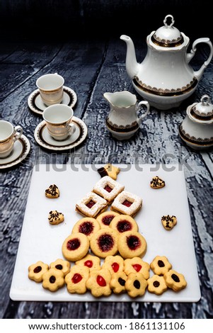 Biscuits and pastries of different flavors, cream, raspberry jam, honey, blueberries, blackberries, strawberries and coconut. Selected focus. Porcelain cups. Dark wood background. Christmas concept.