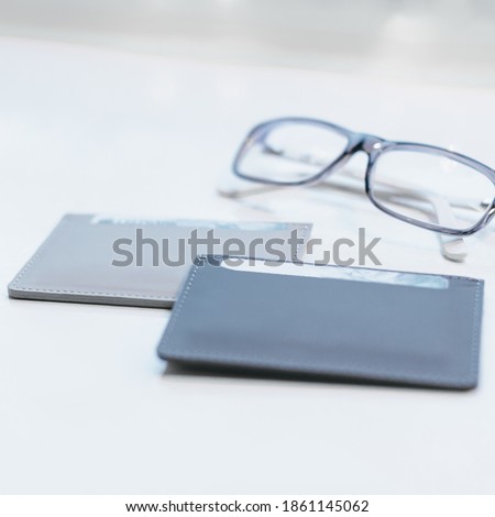 Close up photo of grey modern slim wallets for credit cards and banknotes. Stylish minimalistic accessories from eco leather. On the background blurred glasses. Smooth leather suture.