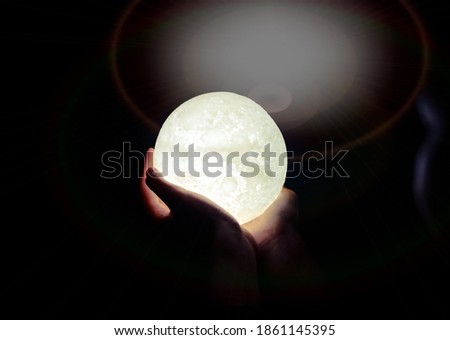 A picture of a hand holding a model of the moon at night and bokeh