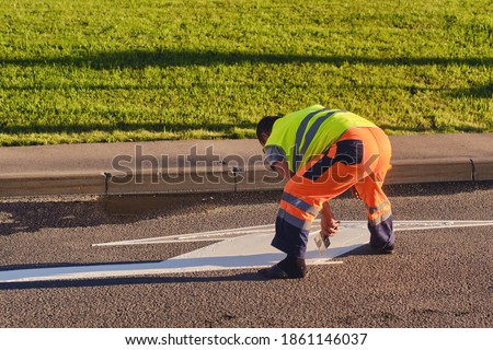 A road worker draws markings on the asphalt with white paint