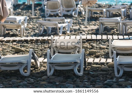Beach white plastic sun loungers on a rocky beach standing in rows Royalty-Free Stock Photo #1861149556