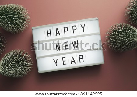 Happy New Year word in light box with Christmas tree top view on pink background