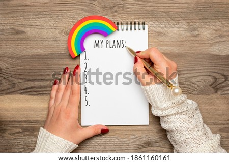 female hand holds pen and writes text 2021 New Year plans on white notepad on wooden background Top view Flat lay Life motivation, idea, success, vision, inspiration, planning concept Holiday card