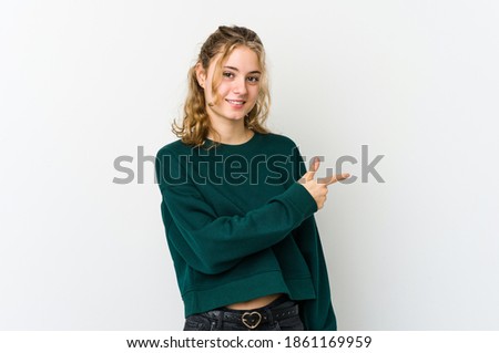 Young caucasian woman on white backrgound smiling and pointing aside, showing something at blank space.
