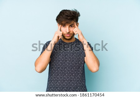 Young arabian man isolated on a blue background focused on a task, keeping forefingers pointing head.