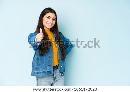 Young indian woman isolated on blue background smiling and raising thumb up