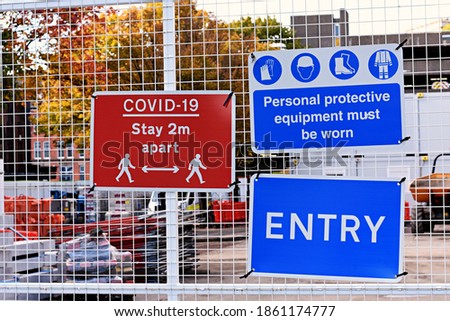 Entrance to a construction site with warning signs attached to a fence. Covid 19 stay 2 metres apart. Personal protective equipment must be worn. Entry.