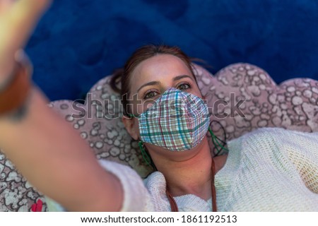 Beautiful woman making a selfie lying down and wearing a mask against the covid19, wearing a jumper and a leather collar. Lifestyle