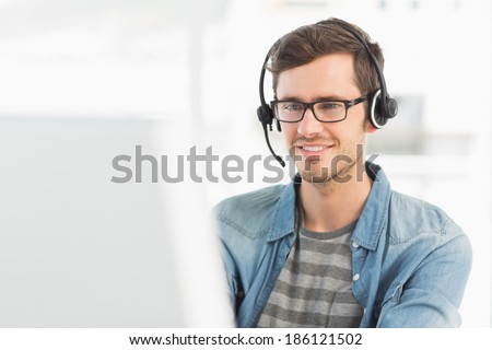 Smiling casual young man with headset using computer in a bright office Royalty-Free Stock Photo #186121502