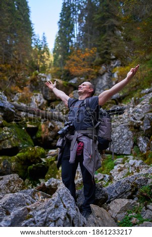 Professional nature photographer with heavy backpack, tripod and camera hiking in the forest and mountains